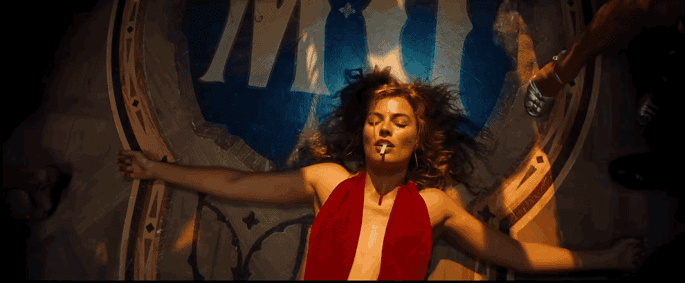 Movie gif: Margot Robbie lying on the floor at a party wearing a scarf-like dress