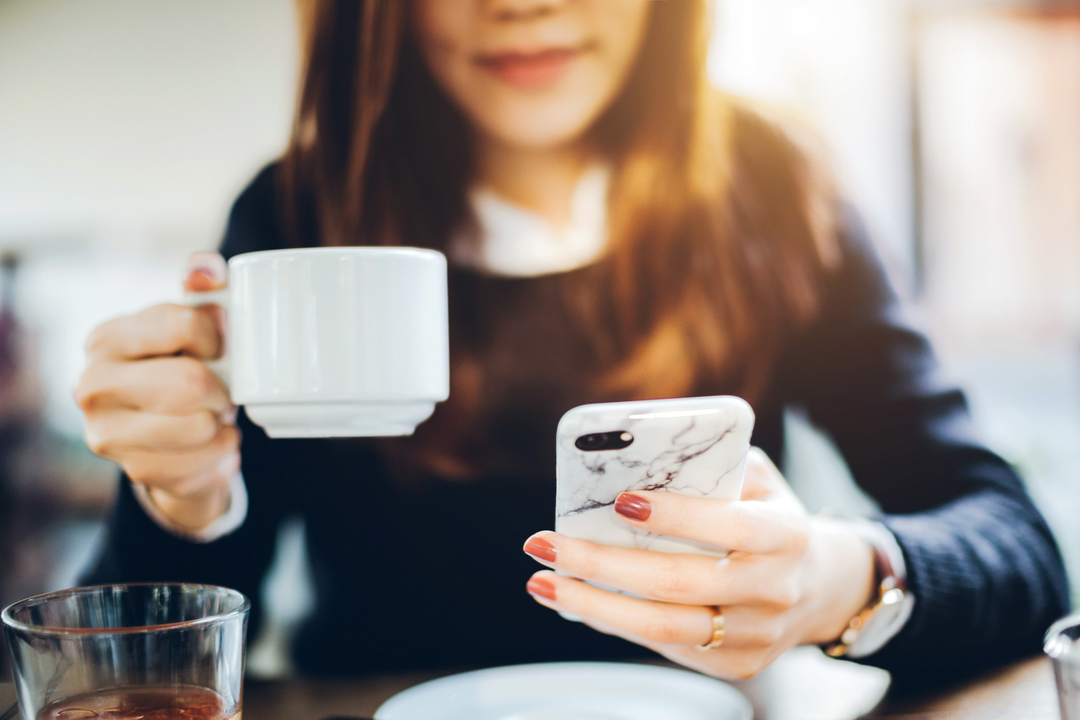 A woman looking at her mobile phone while drinking coffee