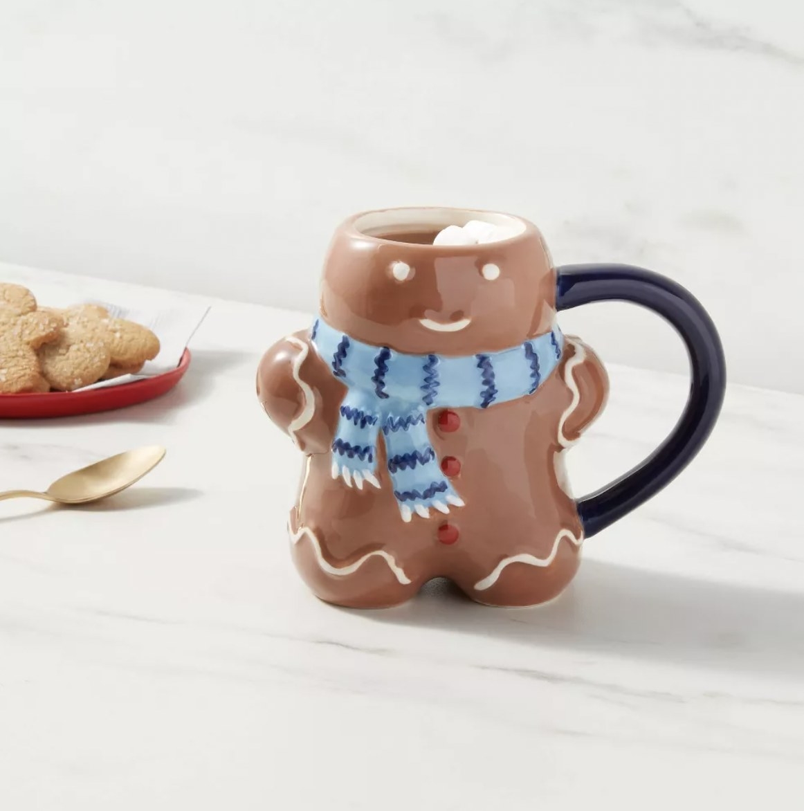 the mug with hot cocoa and marshmallows next to plate of sugar cookies and golden teaspoon