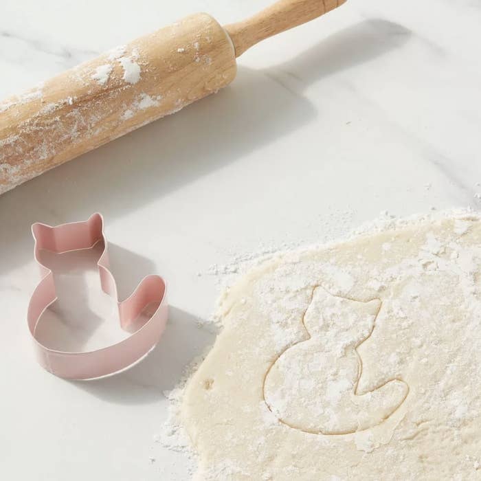 the pink cookie cutter next to dough with the cat shape cut into dough