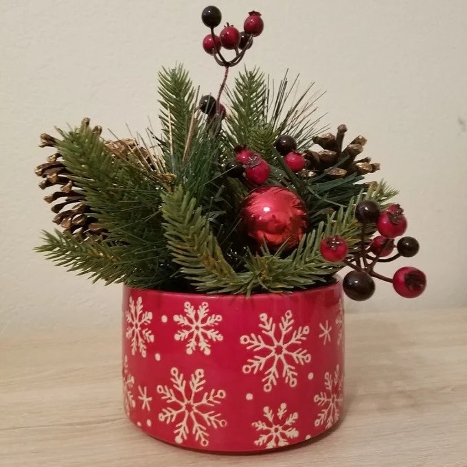 a reviewer photo of the red ceramic pot with white snowflakes on it, christmas pine and berry plant arrangement inside