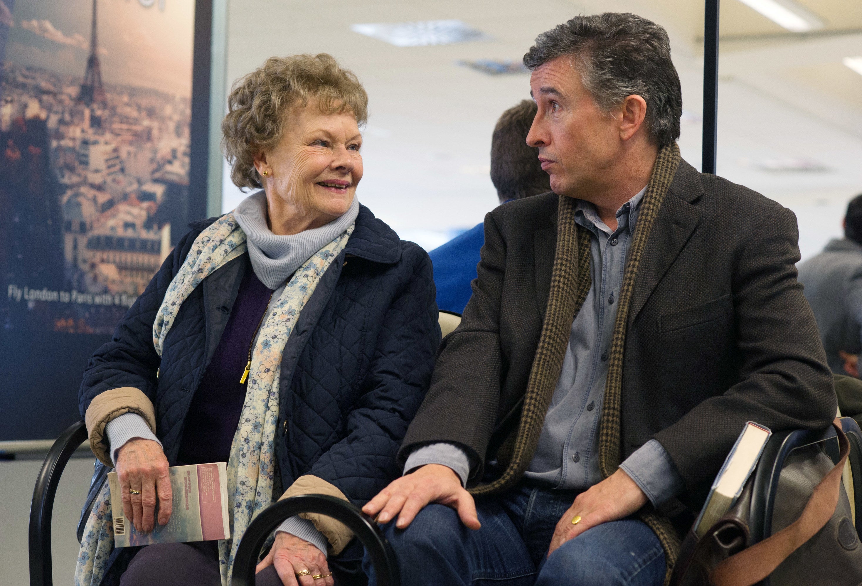 Judi Dench and Steve Coogan sit next to each other at an airport