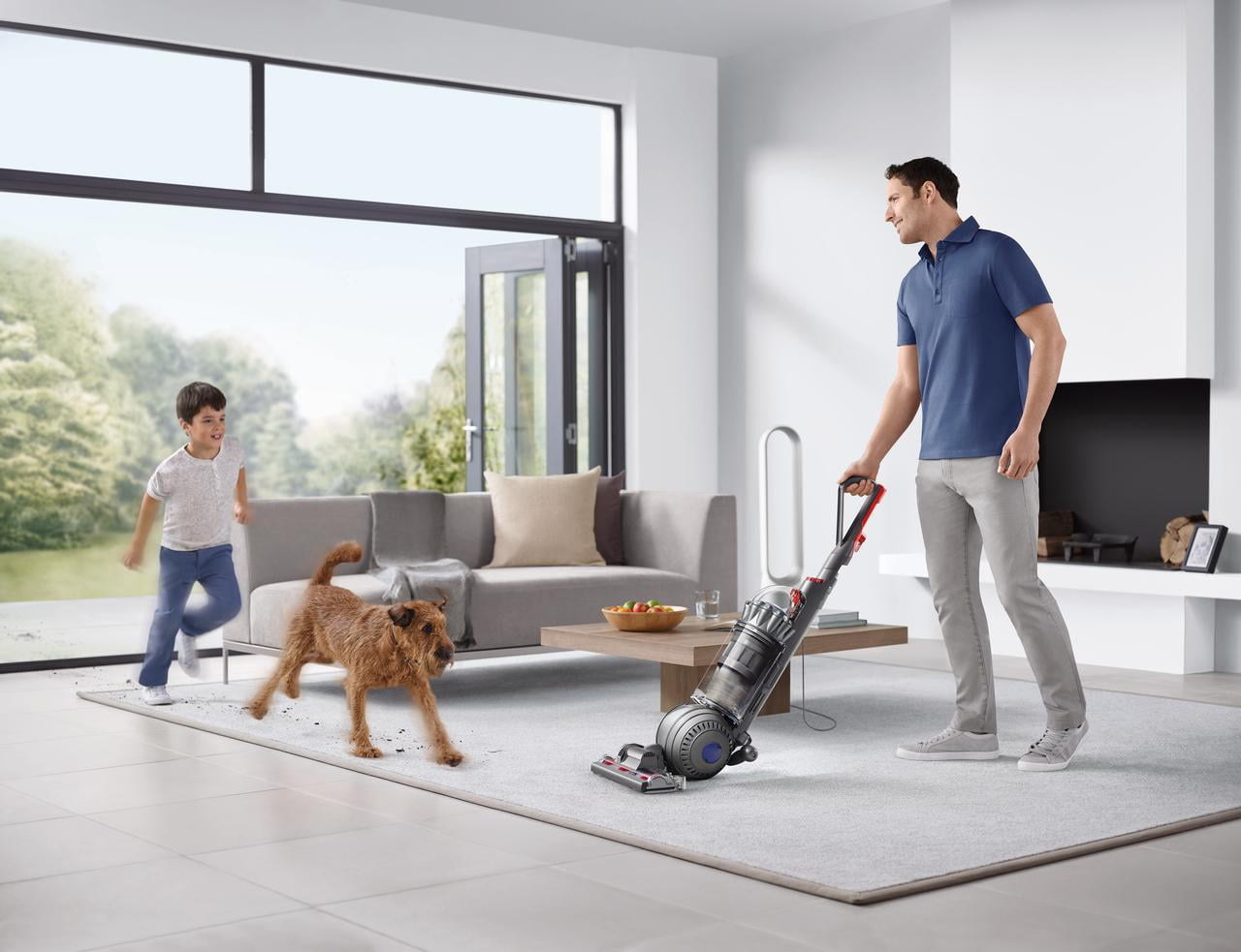 A dad vacuuming while a dog and boy run around