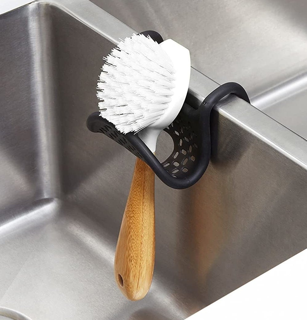 the sink sling slung over a sink while holding a scrubbing brush
