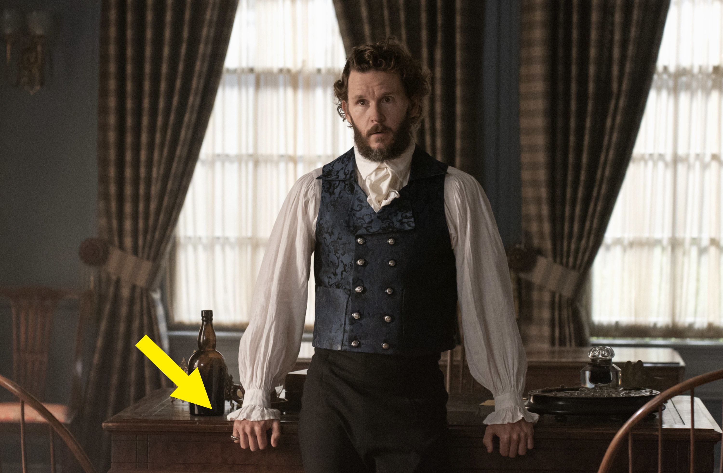 Ryan as Tom leaning against a desk with an arrow pointing at his ring