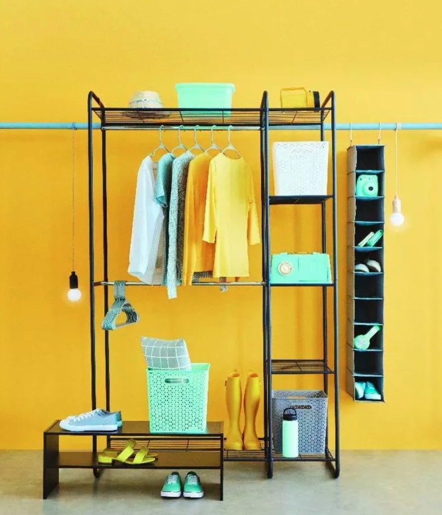 the black metal freestanding closet on a yellow background, filled with yellow and teal clothes and accessories