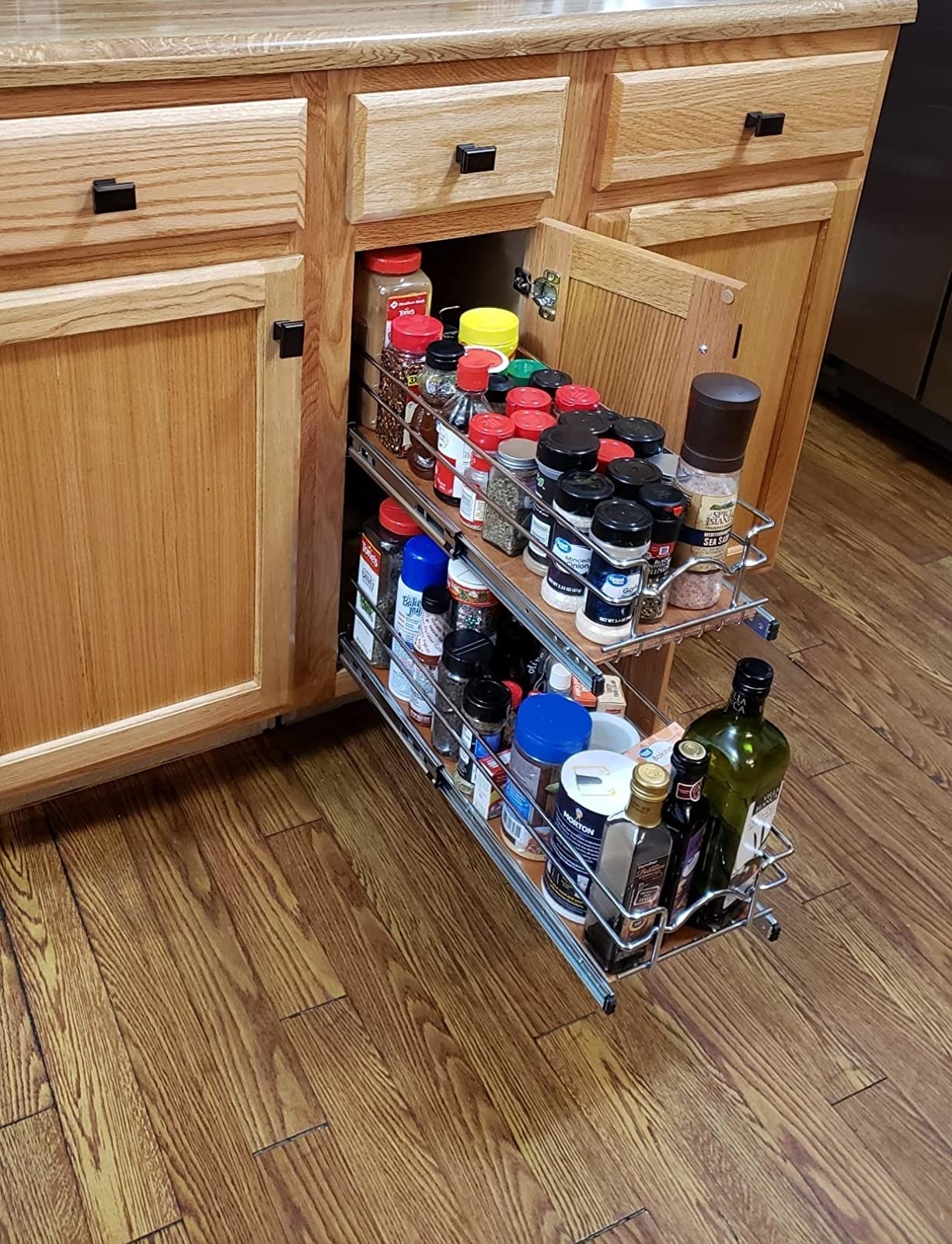 A reviewer&#x27;s wood cabinet with one door open and these two-tier shelves pulled out with spices and other ingredients on them