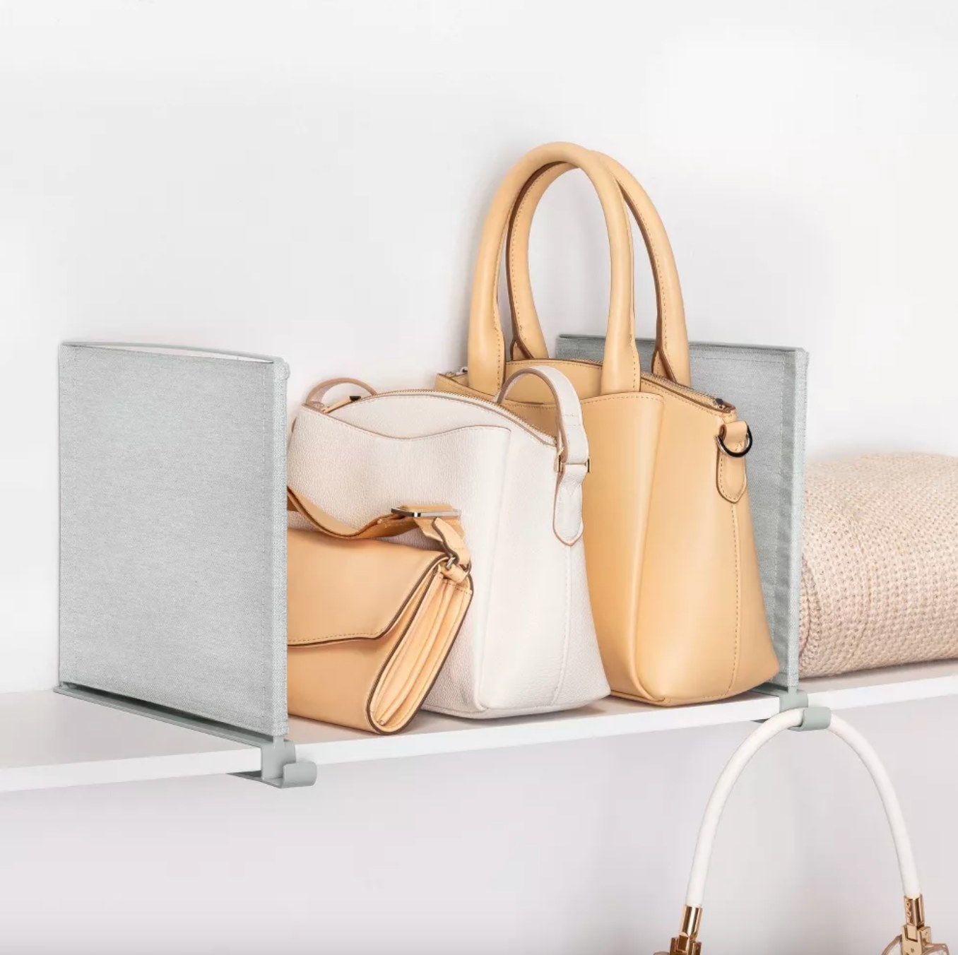 the two grey shelf dividers set up around several tan purses — an additional purse is hanging from the attached hooks on the front of the dividers