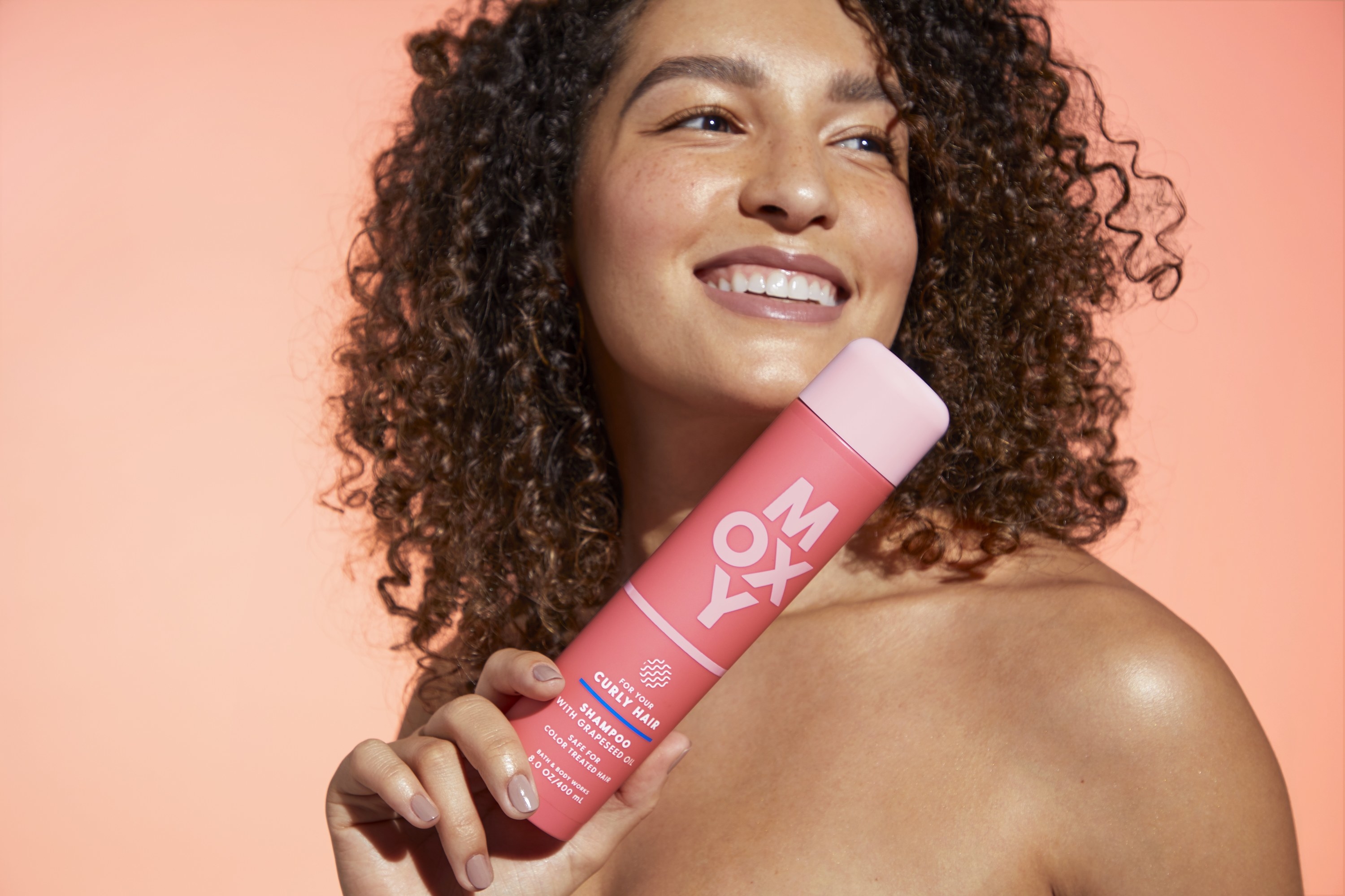 A woman smiling while holding Curly Hair shampoo