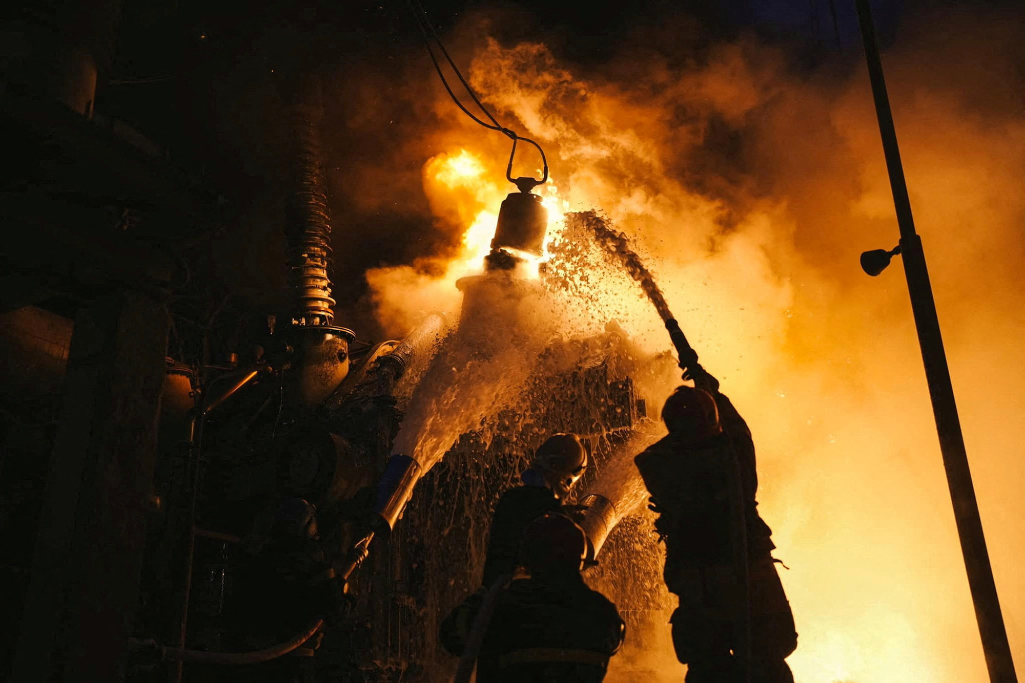 Firefighters pouring water upward at a blazing structure at night