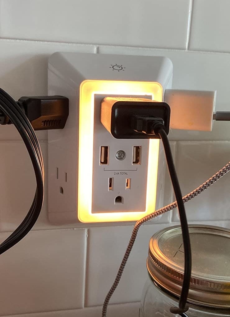 Reviewer pic of the six chargers and two USB chargers with things plugged in to all of them in the lit outlet