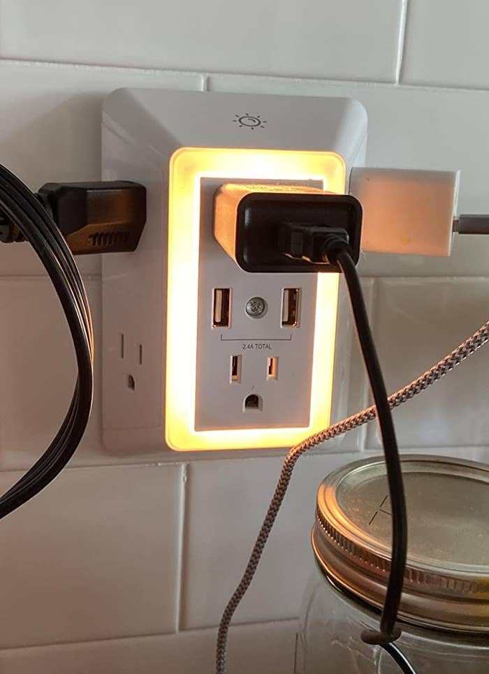 Reviewer pic of the six chargers and two USB chargers with things plugged in to all of them in the lit outlet