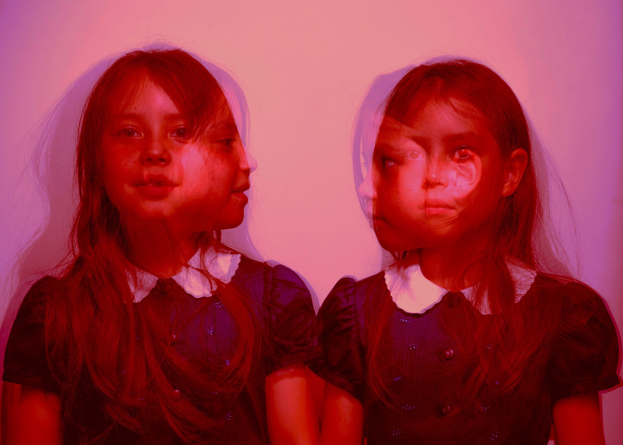 Two young girls looking forward and back at each other in the same image, with a red overlay