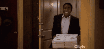 man walks in a room happily with pizza boxes to discover everything is on fire