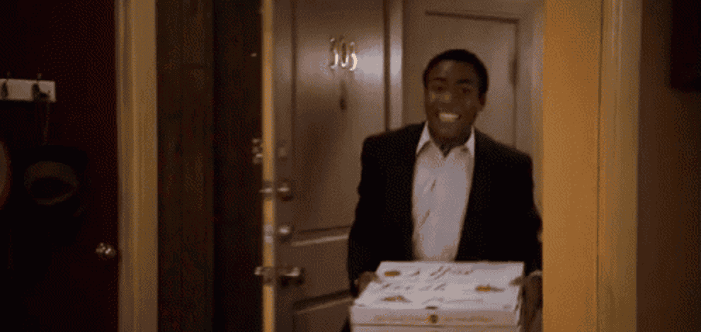 man walks in a room happily with pizza boxes to discover everything is on fire