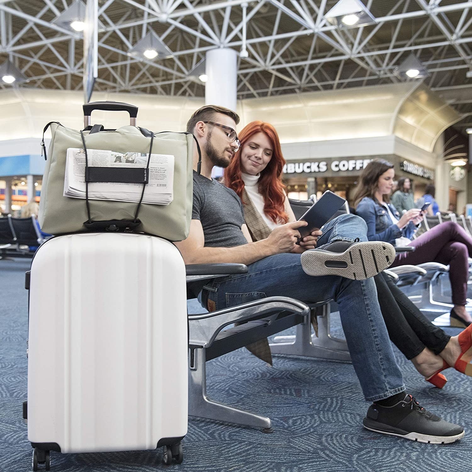 couple sitting on an airport chair with their bag bungeed on their suitcase