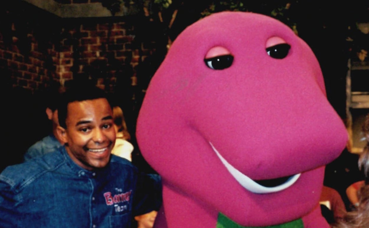 a man standing next to barney the dinosaur