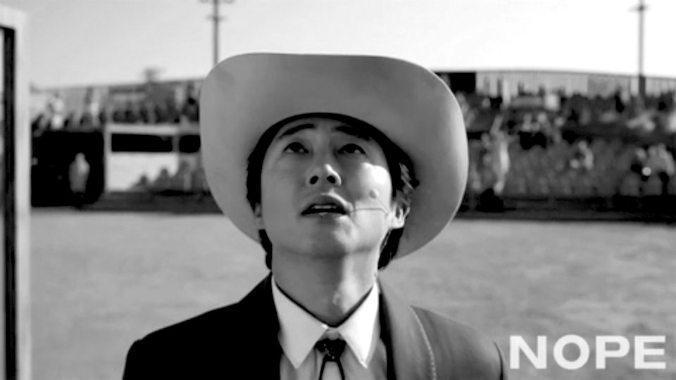 Jupe from Nope in a cowboy hat and suit, looking up