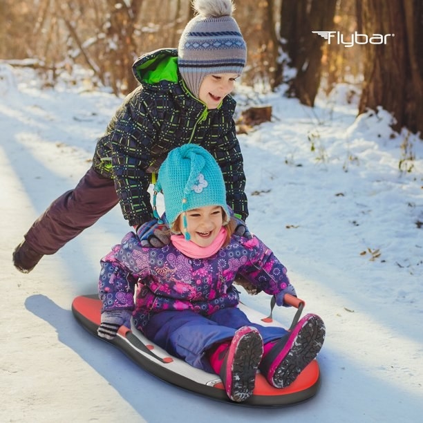 Kid riding on sled with another kid pushing