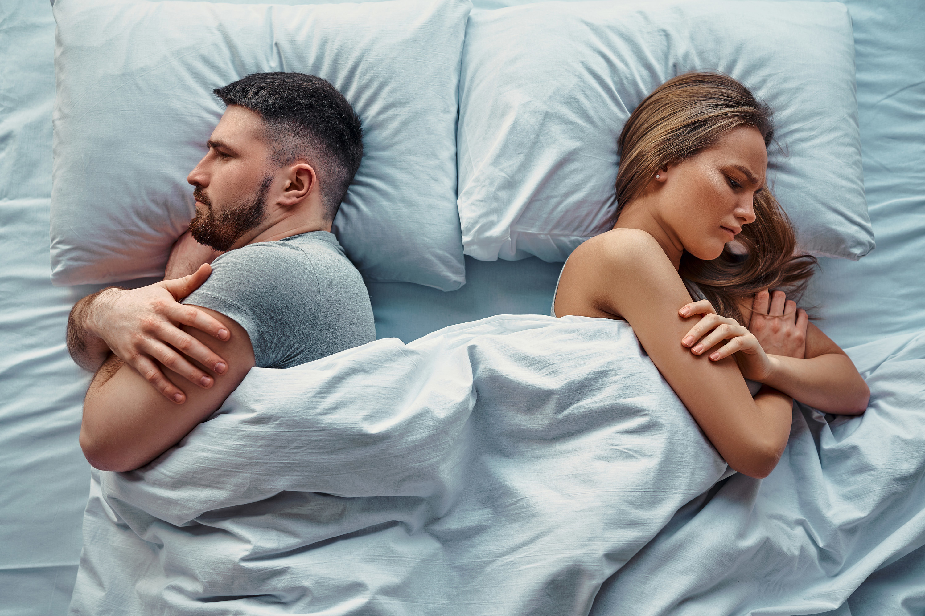 An angry man and woman facing away from each other in bed