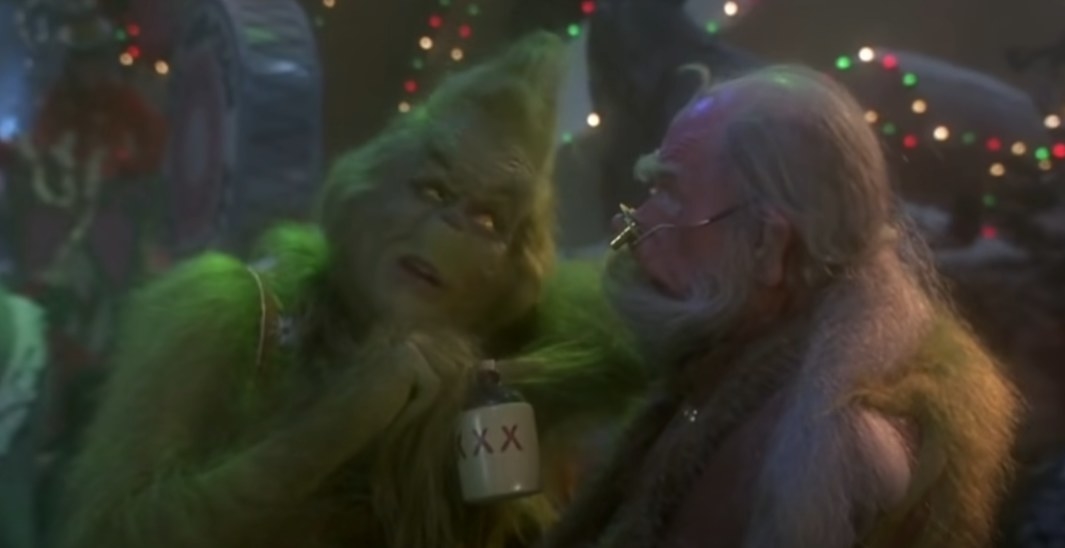 The Grinch leaning into a guy while grabbing his little flask with xxx labeled on it about to drink it