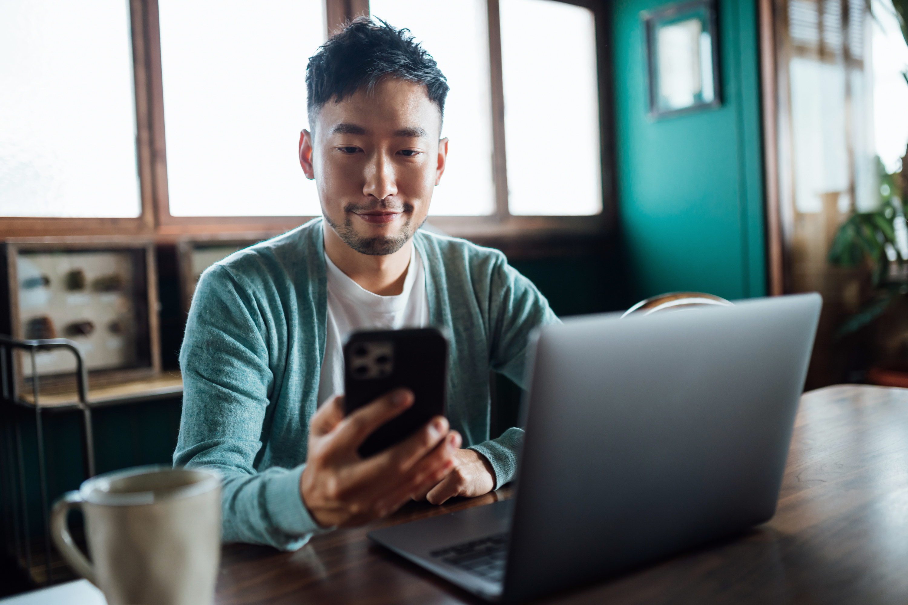 A man looking at his phone in front of a laptop