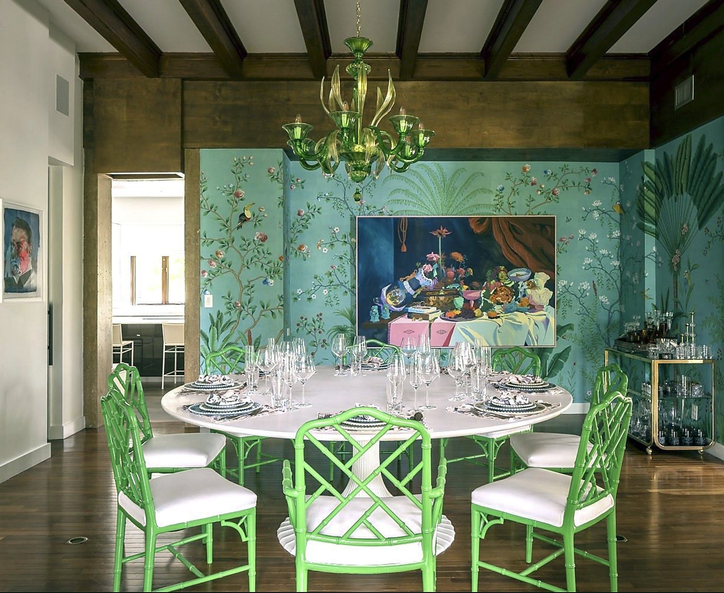 Round dining table with green-accent seats, paintings on the walls, and multi-light green chandelier