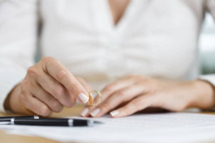 woman taking off her wedding ring to sign divorce papers