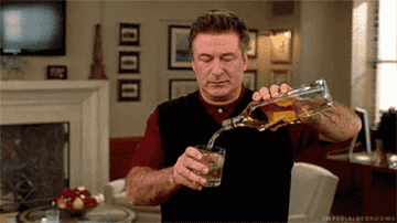 Alec Baldwin pouring a large glass of whiskey
