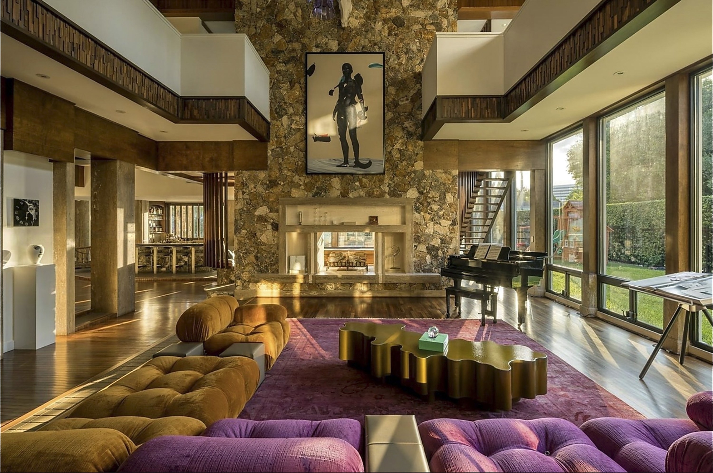 The high-ceiling living room area with sectional plush sofa and piano and floor-to-ceiling windows