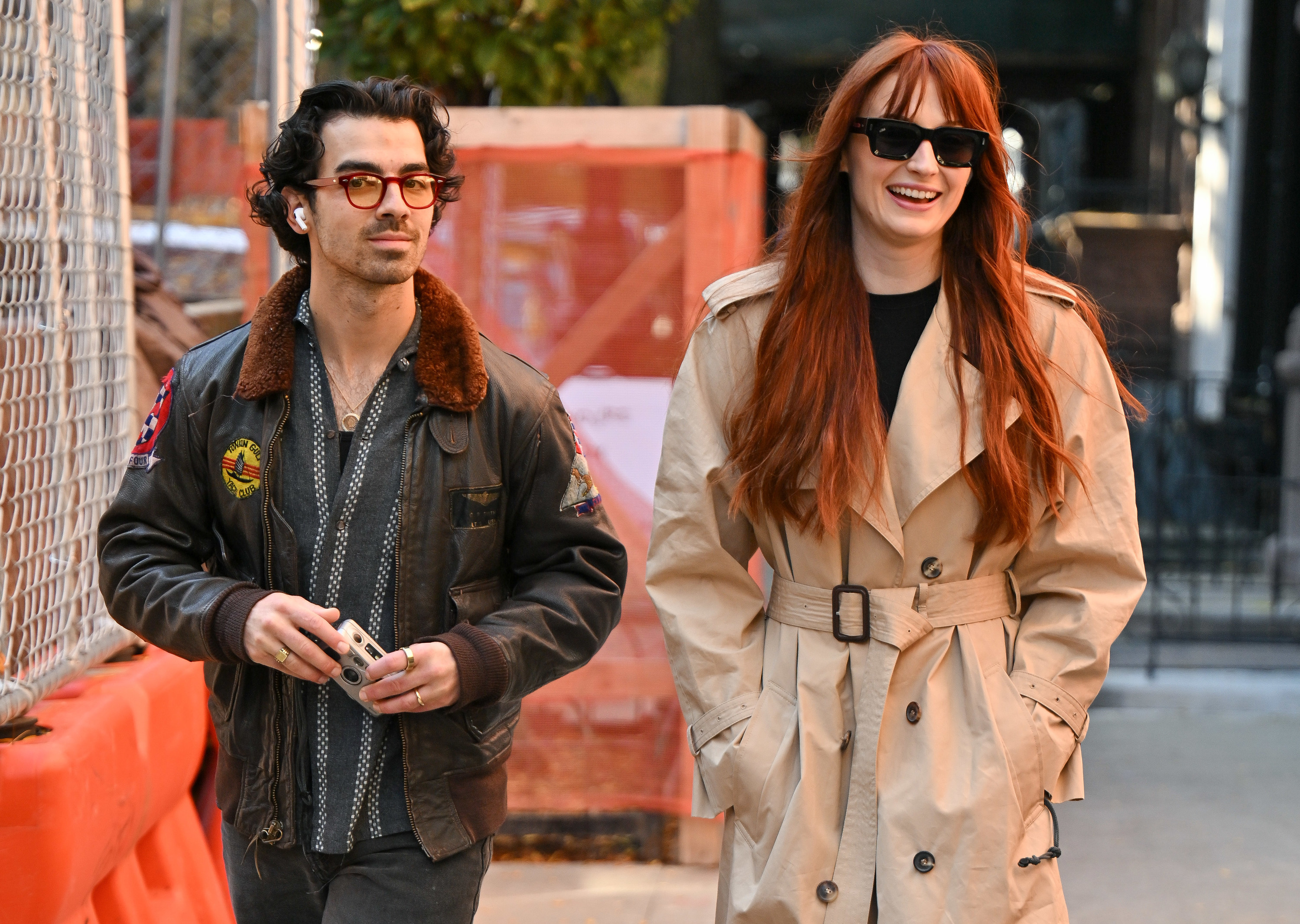 Joe in a leather jacket and Sophie in a trench coat walking on the street