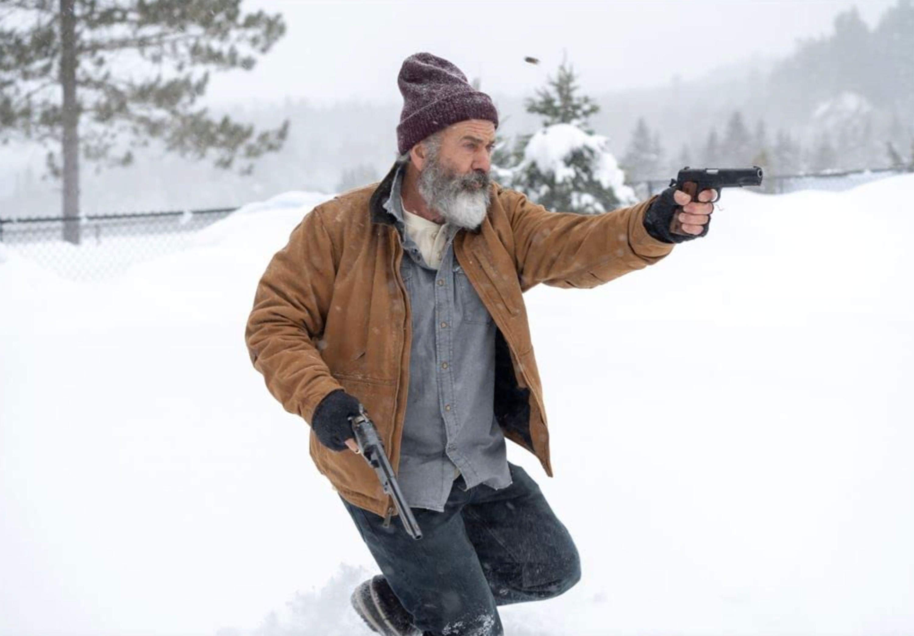 A bearded man in a red beanie wields two pistols at an enemy