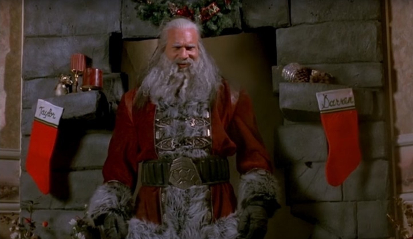 An intimidating Santa Claus stands imposingly in front of a fireplace