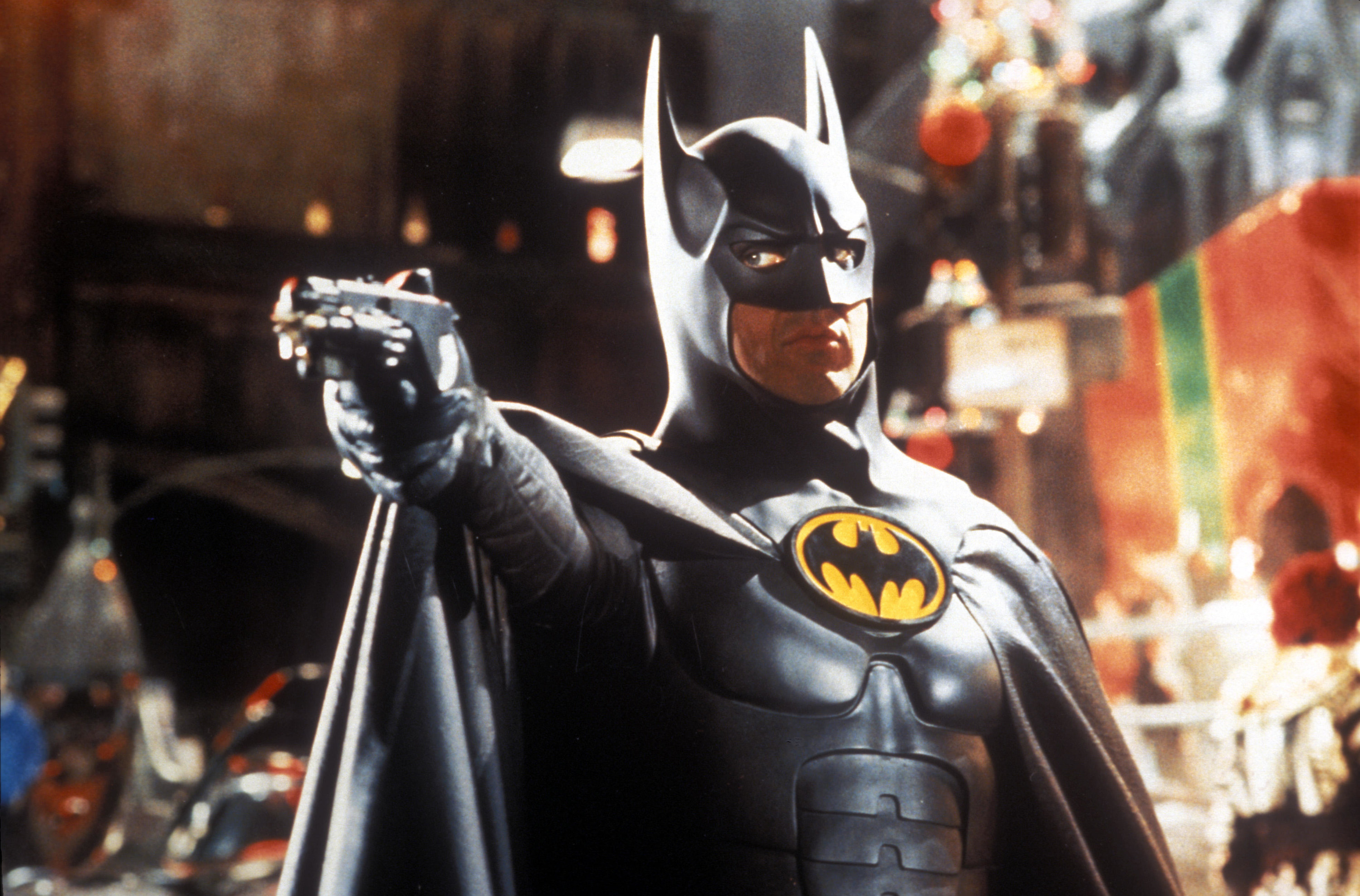 Batman points a gun-like gadget at an enemy at a holiday celebration