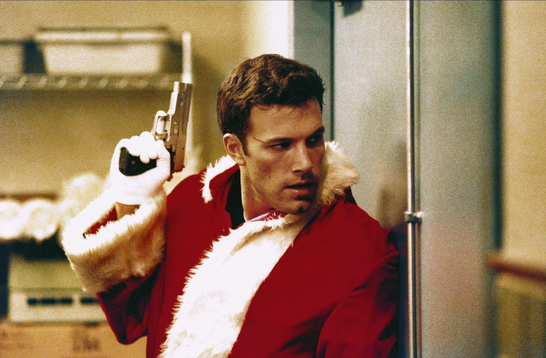 A gun-wielding man in a Santa costume hides from a threat behind a door