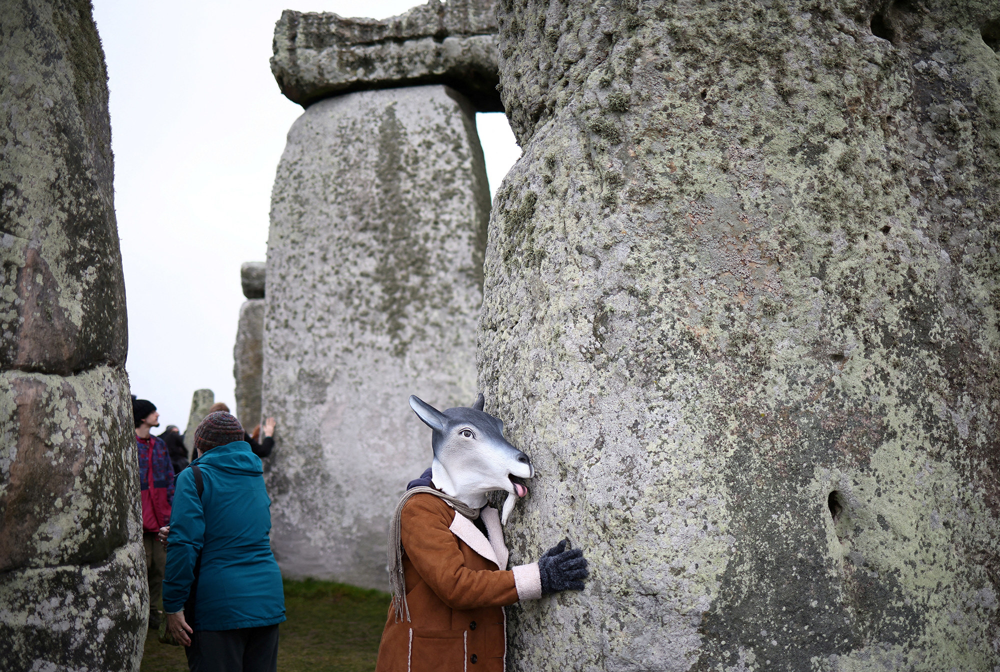 someone in a goat mask hugging a stonehenge rock