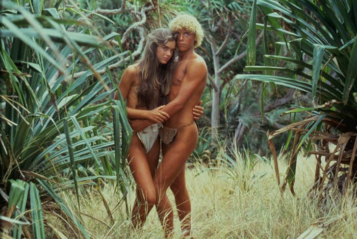Emmeline and Richard embracing amid the grass and wearing just loincloths