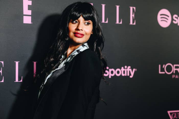 Jameela Jamil, a woman with long black hair in front of a black wall with
pink logos of Elle, Spotify and others. She wears a black blazer and red lipstick. 