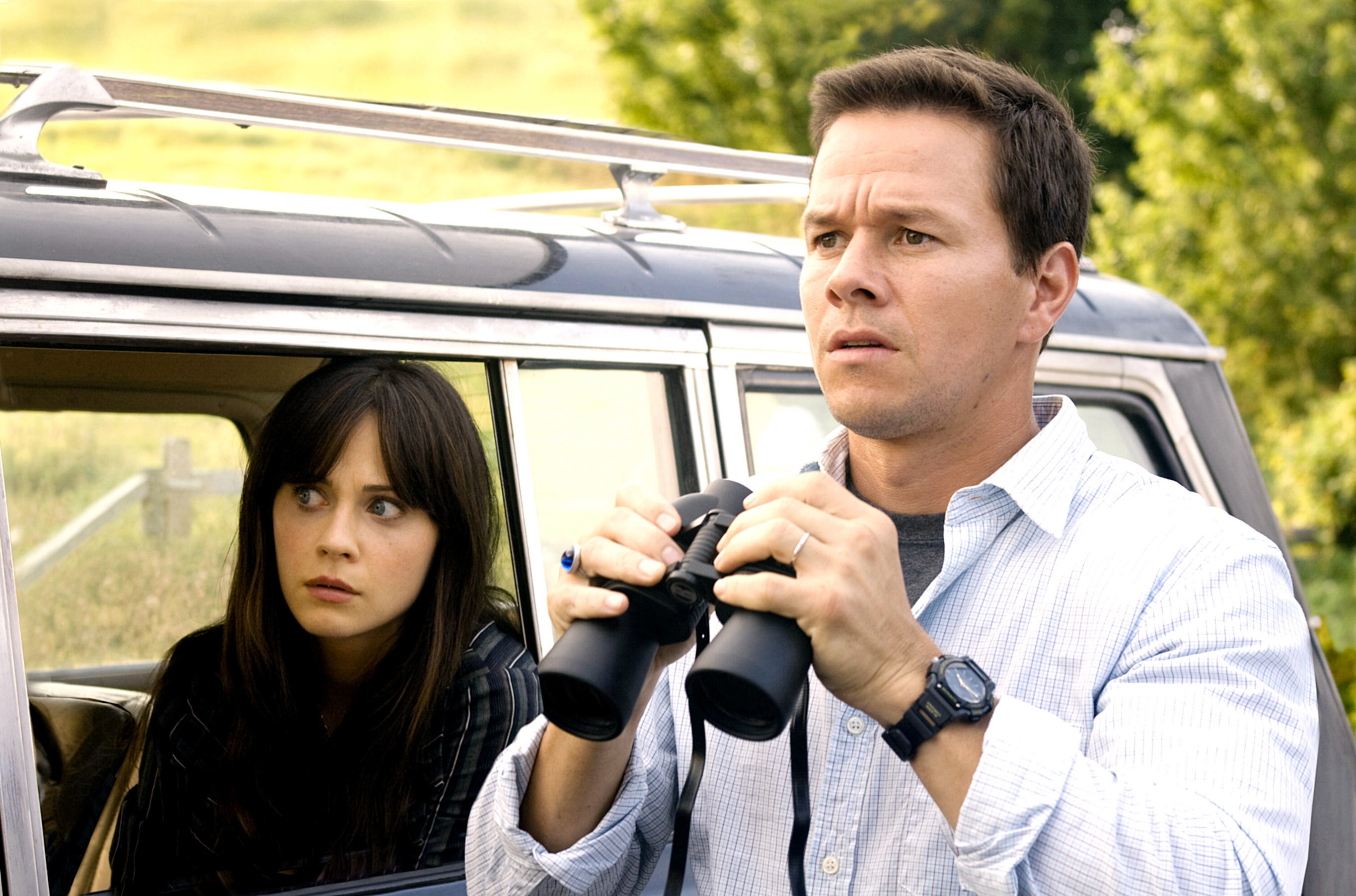 A woman in a car and a man standing next to it holding binoculars
