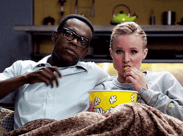Two people sitting on a couch with a bucket of popcorn