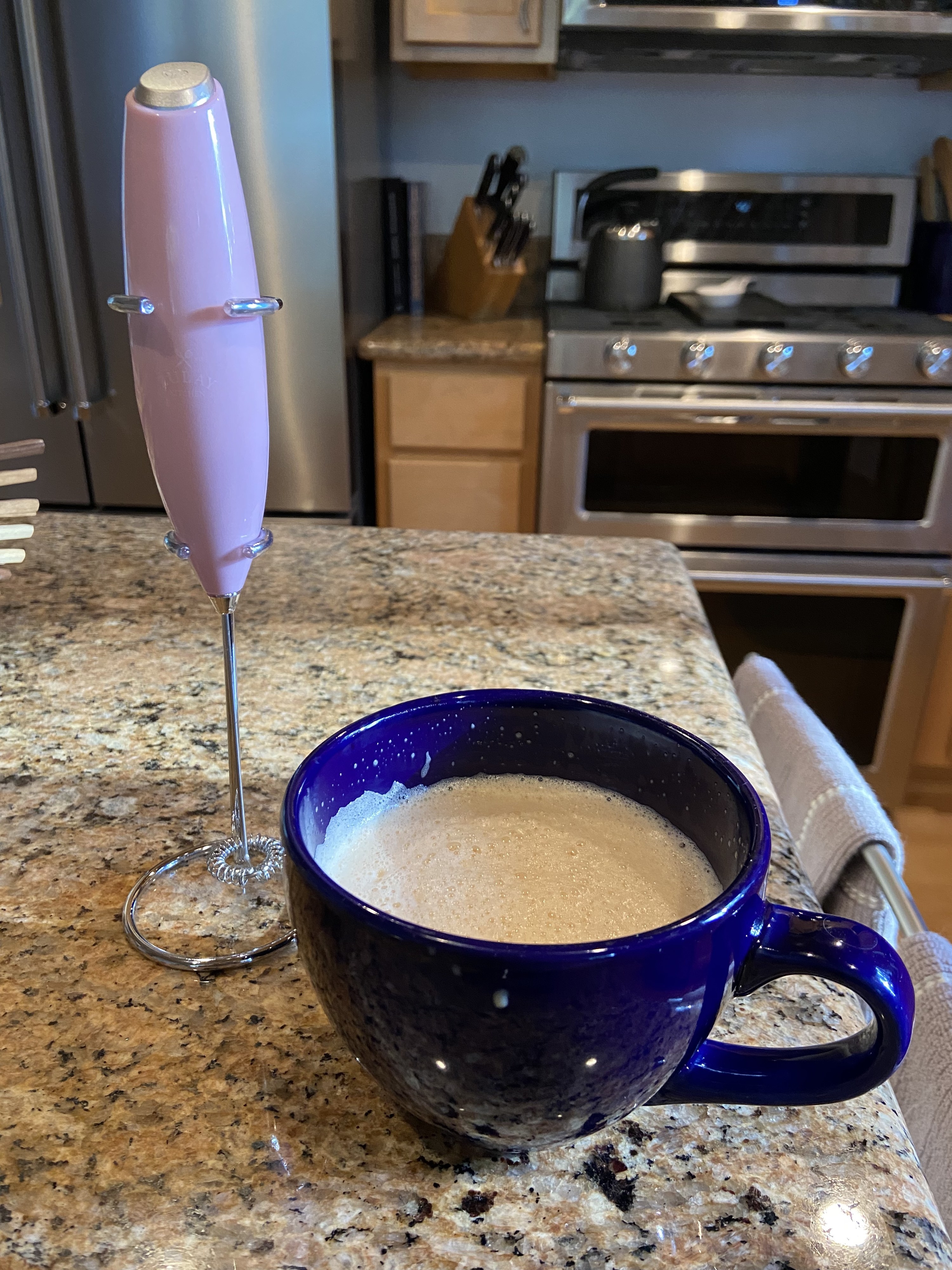 reviewer&#x27;s purple frother next to mug of frothed coffee