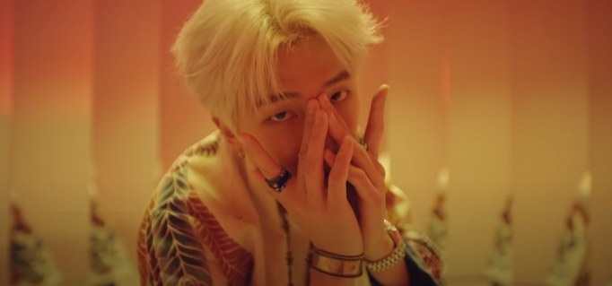 RM covers his face with his hands while looking towards the camera in the Intro: Persona music video