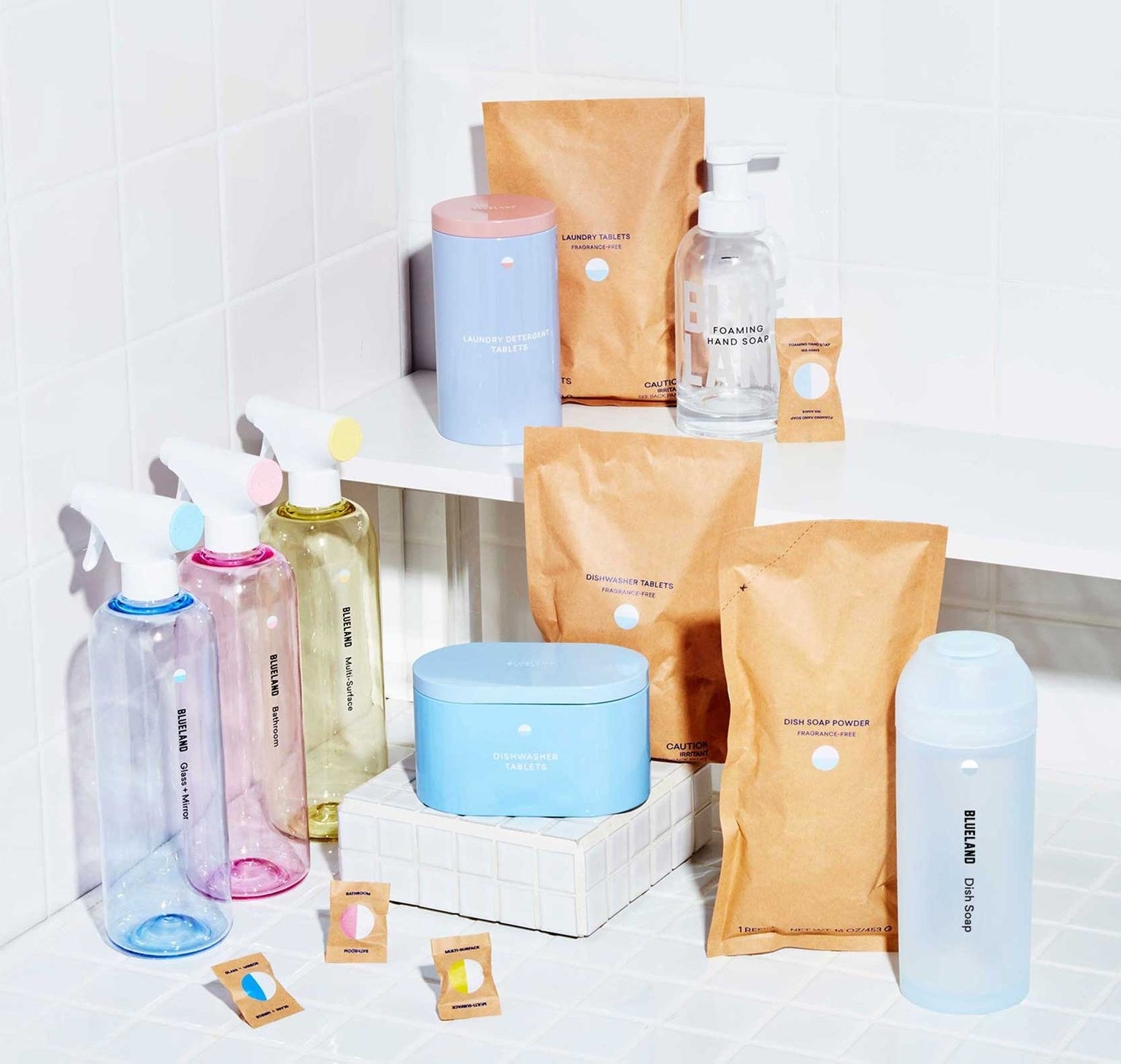 an assortment of cleaning products, multicolored bottles, paper packages, and containers against a white tile background