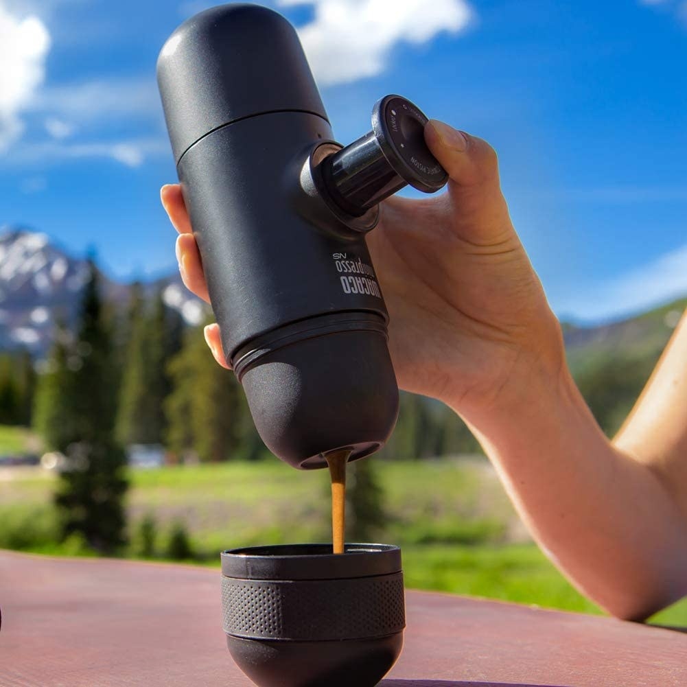 A picture of a person pouring coffee from an espresso machine into a cup at the beach