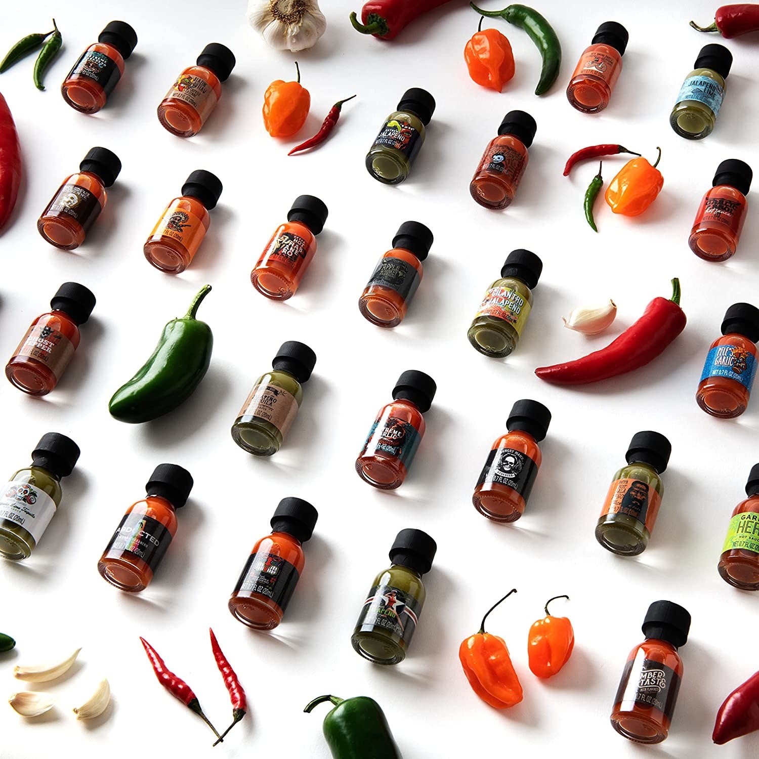 the bottles of hot sauce laid out on a simple background with hot peppers and garlic cloves