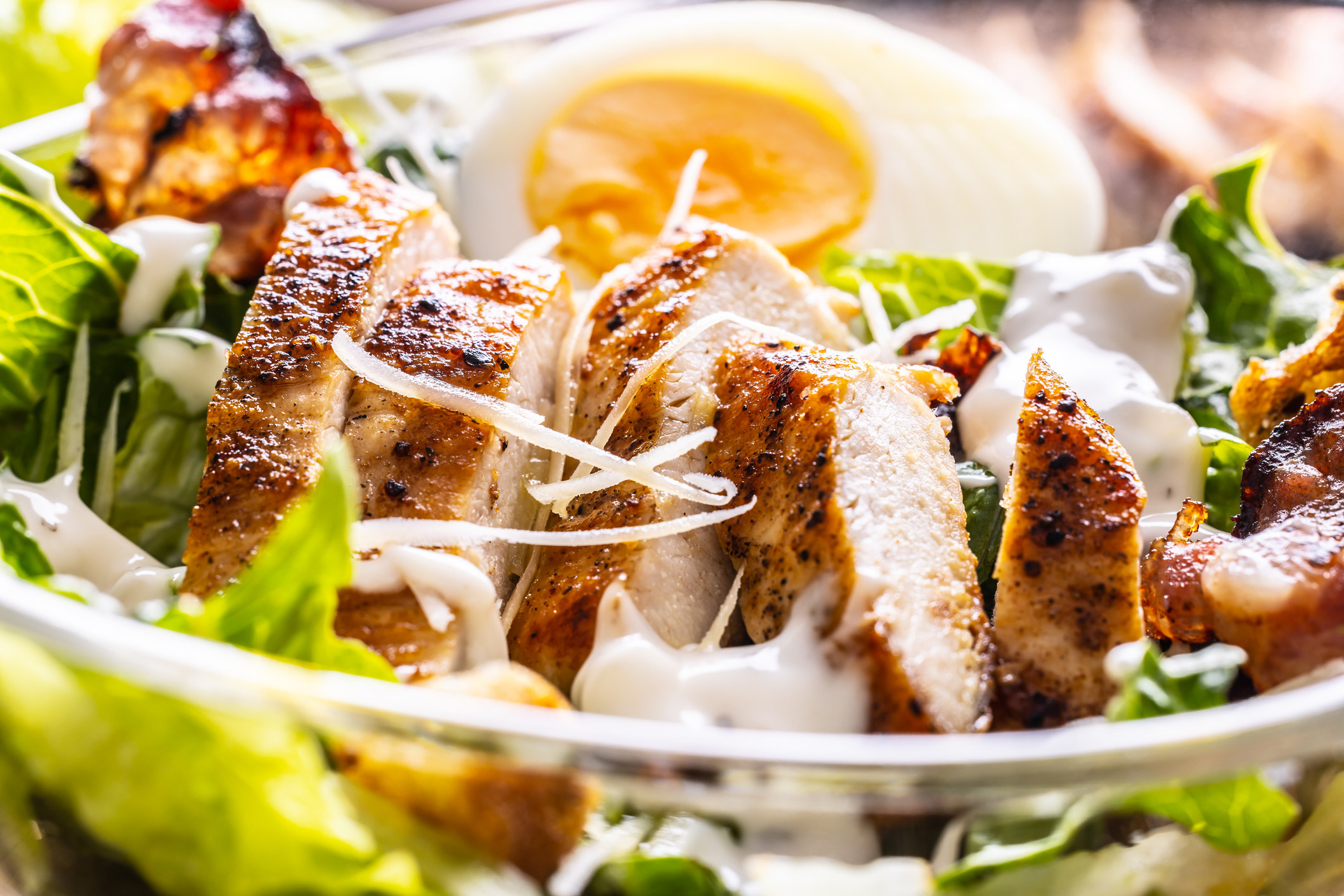 Caesar salad with grilled chicken slices in a glass bowl.