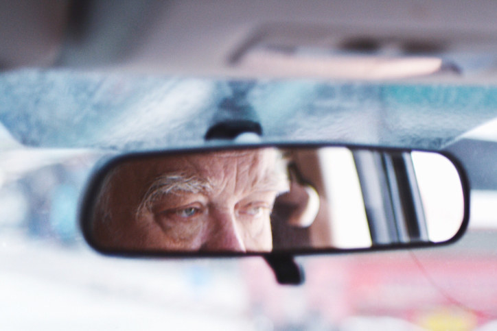 An older man&#x27;s reflection in the rearview mirror