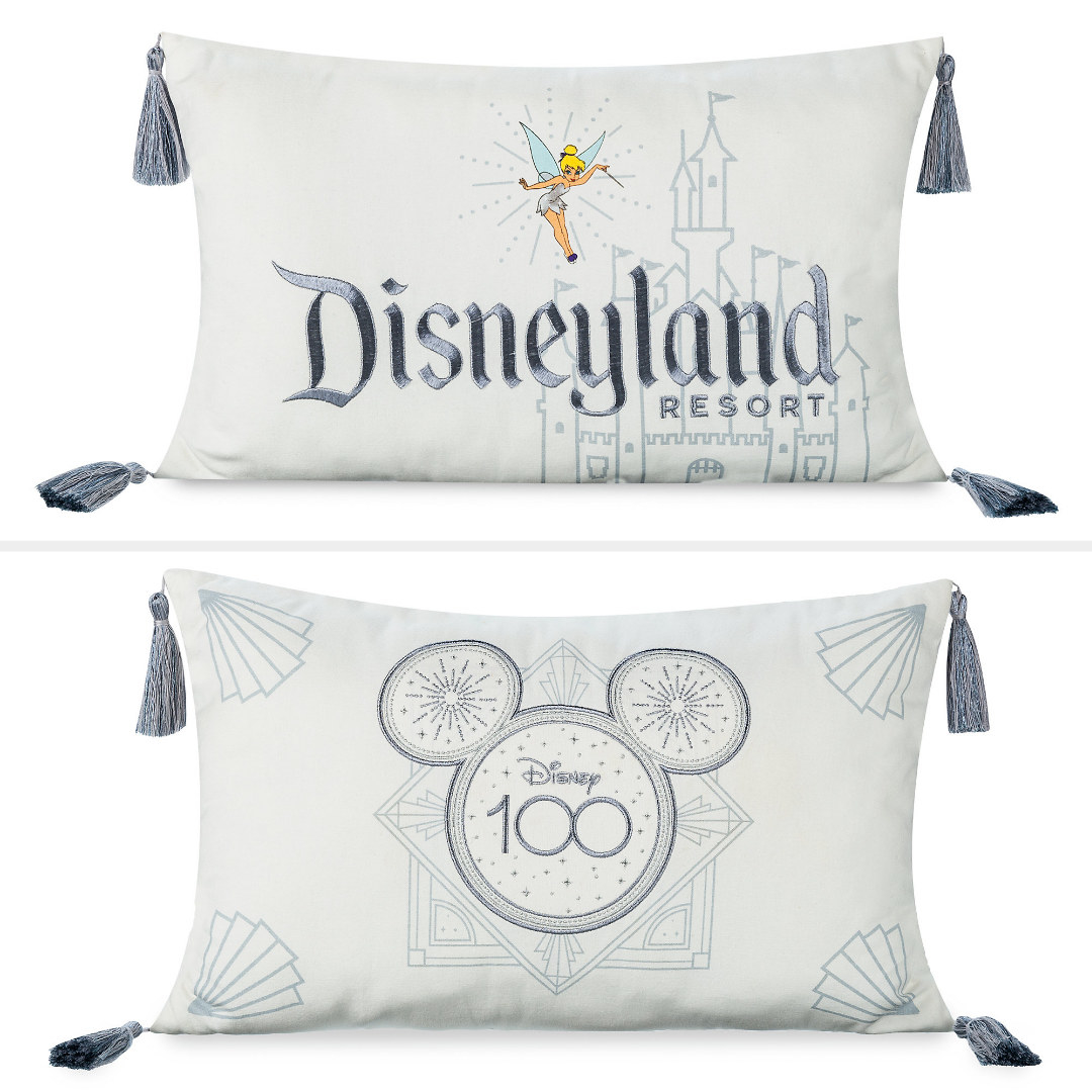 A rectangular white pillow that features artwork of Sleeping Beauty&#x27;s Castle and Tinker Bell in glittering attire, tassel appliques, and &#x27;&#x27;Disneyland Resort&#x27;&#x27; embroidered text