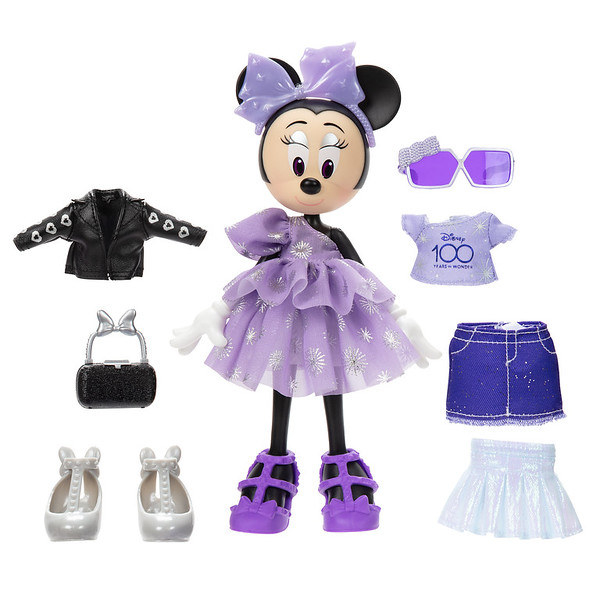 A Minnie Moues doll in an off the shoulder purple dress with sparkles on it and accessories including a leather jacket, purse, change of silver shoes, sunglasses, Disney 100 shirt, jean skirt, and a sparkly iridescent silver skirt