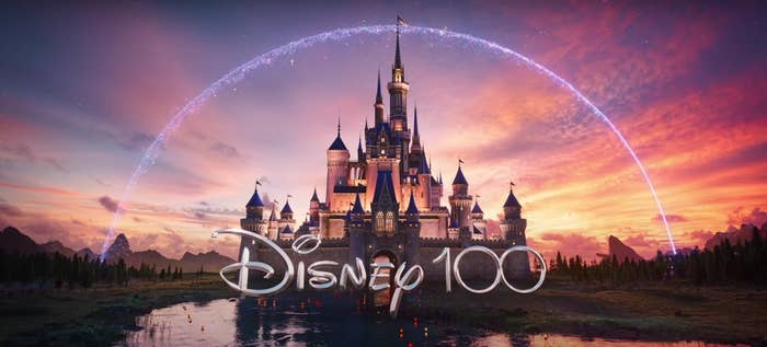 The Disney 100 logo that shows Cinderella&#x27;s castle and Tinkerbell&#x27;s magic fairy dust arching over it and a sunset behind the castle